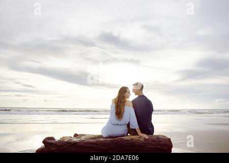 Ein Paar sitzt auf einem toten Baumstamm am Strand In Bali bei Sonnenuntergang Stockfoto
