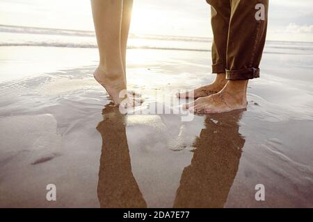 Männerfüße vor den Füßen einer Frau, mit pinkem Nagellack an einem Strand in Bali hebend Stockfoto