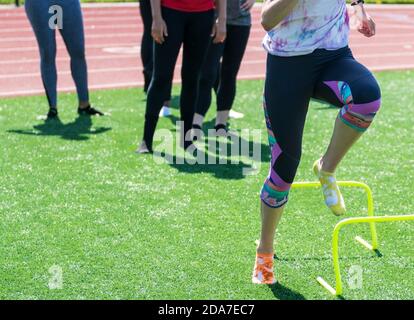 Track Läufer über gelbe Mini-Hürden ohne Schuhe auf Socken auf einem grünen Rasen Feld während der High School-Strecke und Feld üben. Stockfoto