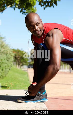 Portrait von fit jungen schwarzen Kerl mit Ohrhörer binden Schuh Schnürsenkel vor einem Lauf Stockfoto