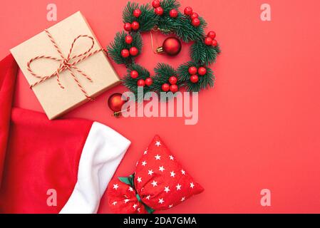 Weihnachtskomposition, Layout auf rotem Hintergrund mit Box, Kranz, Weihnachtsspielzeug und Tasche, Winterurlaub Konzeptbild Stockfoto