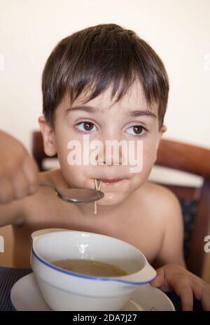 Der kleine Junge isst mit einem Löffel aus dem Teller Stockfoto