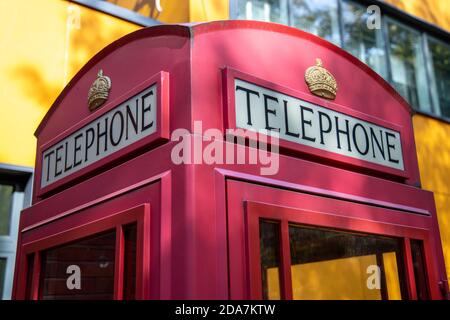 Traditionelle rote britische Telefonbox gegen eine gelbe Wand Stockfoto