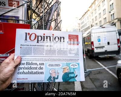 Paris, Frankreich - 9. Nov 2020: POV männliche Hand kaufen an Presse Kiosk l'Opinion Zeitung mit Karikatur von Joe Bidens projizierten US-Präsidentschaftswahlsieg gegen Amtsinhaber Donald Trump Stockfoto