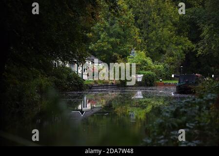 Ein Narrowboot ist in der Nähe einer Hütte über der Schleuse vertäut Bei Deepcut am wunderschönen Basingstoke Canal in Surrey Stockfoto