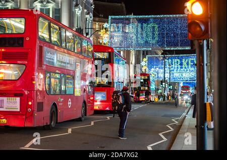 LONDON - 3. NOVEMBER 2020: Rote London Doppeldeckerbusse mit Oxford Street beleuchteten Weihnachtsdekorationen im Hintergrund Stockfoto