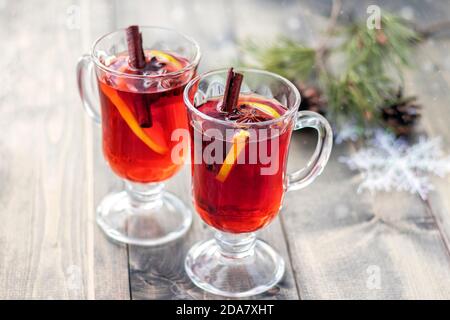 Glühwein zu Weihnachten. Zwei Tassen mit Glühwein auf Holztisch mit verschwommenem Schnee und Zweig von Weihnachtsbaum. Konzept Weihnachten oder Neujahr. Weihnachten. Weichfokus. Stockfoto