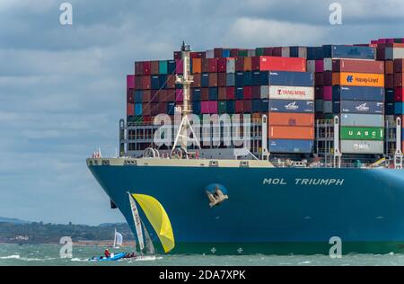 Eine kleine Yacht unter den Bögen eines riesigen Containerschiffes, die MOL Triumph in der solent in den Hafen von southampton vor cowes auf der Insel wight, Stockfoto