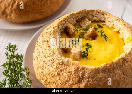 Kürbispüree-Suppe auf einem Teller Brot, Kürbissuppe mit Thymian, Käse und Croutons auf weißem Holzhintergrund Stockfoto