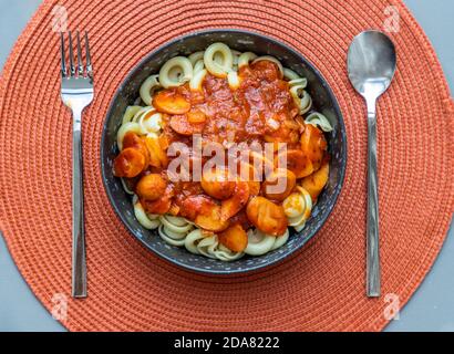 Dischi Pasta mit Wurst, Zwiebel und Balognese Sauce in einem schwarzen Teller auf rotem Hintergrund. Kopierbereich, kein Fokus, speziell. Stockfoto