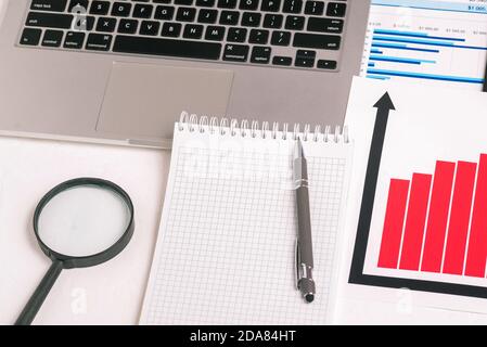 Schreibtisch mit Laptop, Finanzkarte, Buchhaltungsunterlagen und leerer Notizblock-Seite für Text. Das Konzept der Forschung und Analyse des Bestands Stockfoto