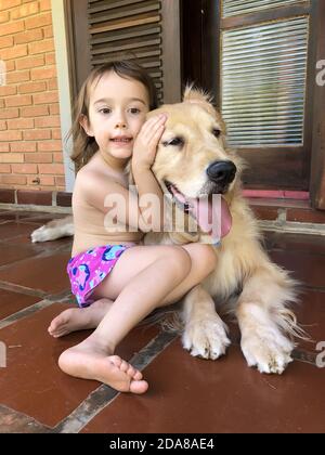 Ein kleines Mädchen umarmt ihren Golden Retriever an einem Sommertag. Stockfoto