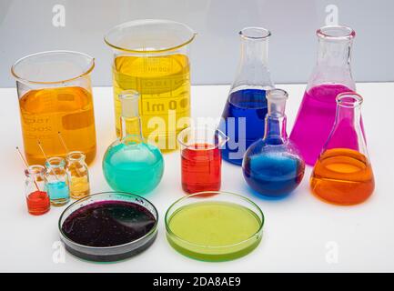 Laborglas mit Flüssigkeiten in verschiedenen Farben auf weißem Tisch. Volumetrische Laborgläser auf weißem Hintergrund. Stockfoto