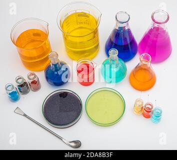 Laborglas mit Flüssigkeiten in verschiedenen Farben auf weißem Tisch. Volumetrische Laborgläser auf weißem Hintergrund. Stockfoto