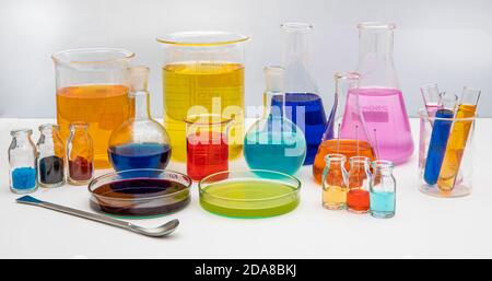 Laborglas mit Flüssigkeiten in verschiedenen Farben auf weißem Tisch. Volumetrische Laborgläser auf weißem Hintergrund. Stockfoto