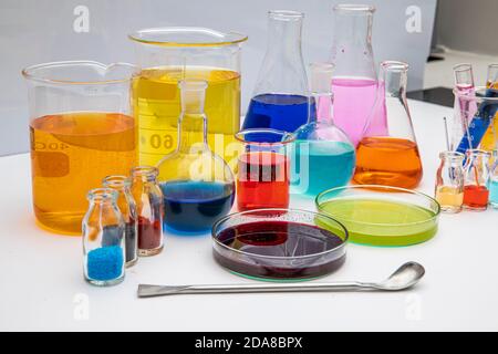 Laborglas mit Flüssigkeiten in verschiedenen Farben auf weißem Tisch. Volumetrische Laborgläser auf weißem Hintergrund. Stockfoto