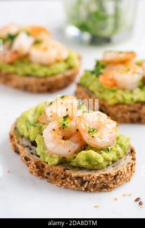 Bruschetta mit Avocado-Creme und Garnelen auf weißem Marmorboden, Nahaufnahme. Vorspeise oder Snack Avocado Toasts mit Garnelen Stockfoto