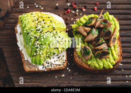 Zwei Toasts mit Avocado, Frischkäse und Pilzen, garniert mit Sesamsamen. Draufsicht. Gesunde Avocado-Toasts zum Frühstück, Mittagessen oder Snack Stockfoto
