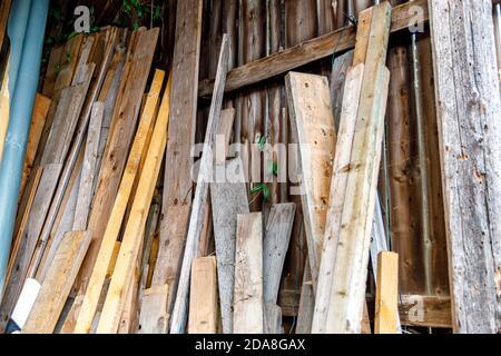 Holzbretter in verschiedenen Größen und Farben lehnten sich mit Holzmaterialien an eine Wand-, Scheune- oder Garagenszene. Stockfoto