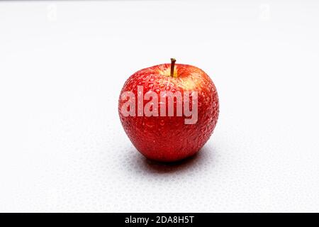 Ein roter Apfel mit einer typischen Apfelstruktur mit gelben und grünen Flecken auf gleichmäßigem weißem Hintergrund, kleine Wasserspritze auf weißem Hintergrund. Stockfoto