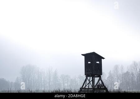 Dunkel und gruselig Holz hoher Sitz für die Jagd auf ein Kalt frostig launisch neblig Wintertag mit Licht Sonnenlicht scheint Durch die Wolken Stockfoto