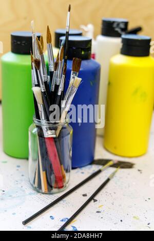Nahaufnahme eines Kunststudios oder Künstlerraums, Bild zeigt Pinsel in einem Glas Becher mit Flaschen von Acrylfarben Stockfoto