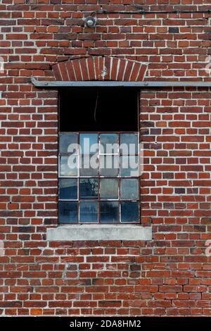 Gebrochene beschädigte Industriefenster mit einem verrosteten Metallrahmen, einige Teile sind weiß lackiert, auf einer roten Ziegelwand, verwenden als Spiel Textur Asset Stockfoto