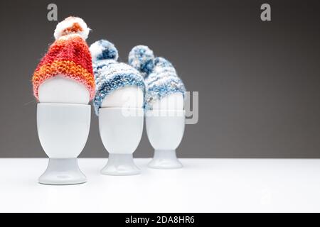 Drei Eierbecher in einer Reihe mit einer blauen und orangen Wollmütze auf dunkelgrauem Hintergrund gekleidet und auf einen Tisch gelegt, verwenden Sie für ostern Grußkarte oder c Stockfoto