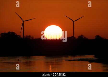 Wittenberge, Deutschland. November 2020. Das Licht der untergehenden Sonne hinter Windkraftanlagen färbt den Himmel und das Wasser der Elbe rot. Quelle: Soeren Stache/dpa-Zentralbild/ZB/dpa/Alamy Live News Stockfoto