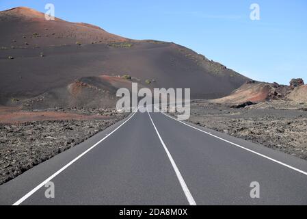 In der Vulkanlandschaft Lanzarotes verschwindet eine Straße in die Ferne Stockfoto