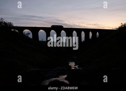 DRS-Lokomotive der Baureihe 37 37407 über das Viadukt von Arten Gill, Dentdale auf der malerischen Eisenbahnlinie Carlisle, die bei Sonnenuntergang eine Silhouette macht Stockfoto