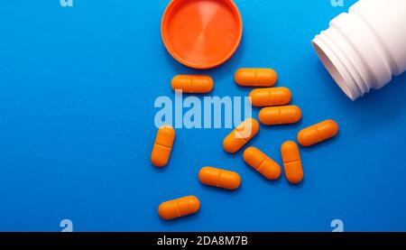 Orangene medizinische Pillen und Tabletten, die aus einer Drogenflasche verschüttet werden. Makro-Ansicht von oben nach unten mit Kopierbereich. Pillen auf blauem Hintergrund. Seitenansicht Stockfoto