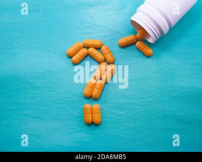 Eine Menge von orangen Pillen auf einem blauen Hintergrund verstreut. Ein Fragezeichen aus Pillen. Gefälschte Arzneimittel. Leeres Leerzeichen zum Einfügen von Text Stockfoto