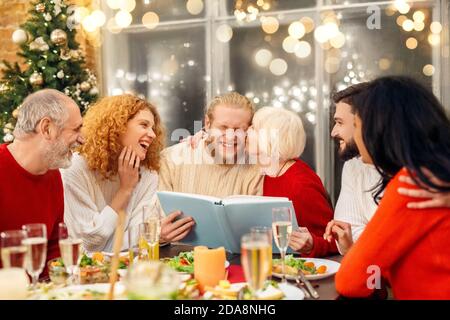 Großmutter sitzt hinter weihnachtstisch, küssen Enkel Stockfoto