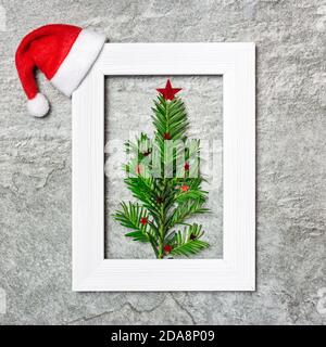 Minimalistischer Weihnachtsbaum aus immergrüner Pflanze in weißem Fotorahmen. Kreative flache Lay-Komposition. Winterurlaub Konzept. Stockfoto