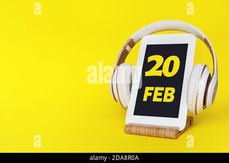 Februar. Tag 20 des Monats, Kalenderdatum. Elegante Kopfhörer und modernes Tablet auf gelbem Hintergrund. Leerzeichen für Text. Bildung, Technologie, Leben Stockfoto