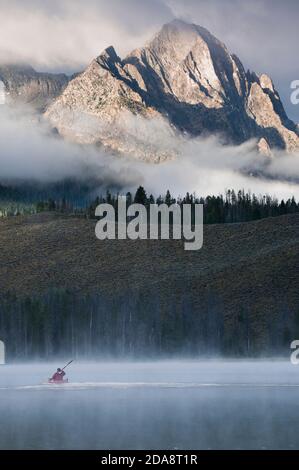 Ein Kajakfahrer paddelt durch den Nebel auf Little Redfish Lake unterhalb der Sawtooth Mountains in Stanley, Idaho. Stockfoto