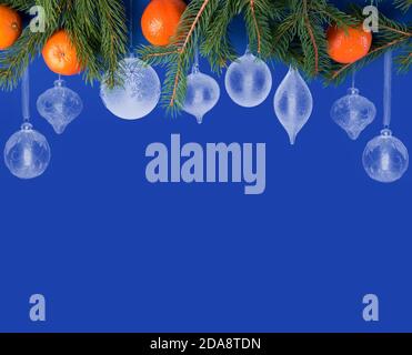 Blauer Weihnachtshintergrund mit dekorierten Rand von weißen Weihnachtskugeln In verschiedenen Formen und mit Fichtenzweigen und Mandarinen Stockfoto