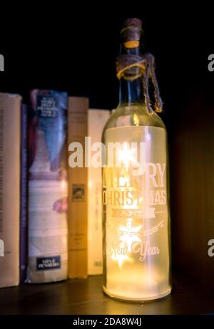 Weihnachtsbeleuchtung Flasche auf einem schwarzen Bücherregal Stockfoto