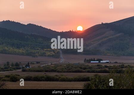 Die Sonne untergeht in trüben Himmel von wildem Rauch in einem Ranching Tal im ländlichen Idaho. Stockfoto
