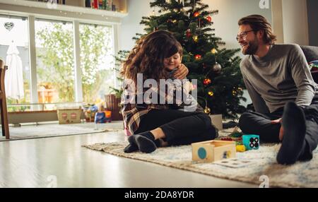 Kleine Familie, die an Weihnachten eine schöne Zeit zusammen hat. Liebende skandinavische Familie sitzt am Weihnachtsbaum zu Hause. Stockfoto
