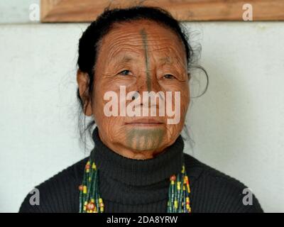 Ältere nordöstliche indische Apatani ethnische Minderheit Stammesfrau mit schwarzen hölzernen Nasenstopfen und traditionellen Gesichts-Tattoos Posen für die Kamera. Stockfoto