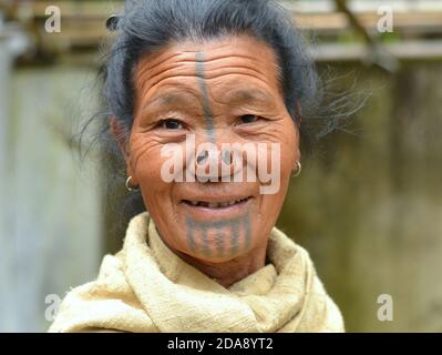 Ältere nordöstliche indische Apatani ethnische Minderheit Stammesfrau mit schwarzen hölzernen Nasenstopfen und traditionellen Gesichts-Tattoos lächelt für die Kamera. Stockfoto