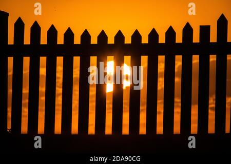 Sonnenuntergang und ein Zaun. Generisches Foto der Sonneneingangsaufnahme durch einen Pfostenzaun. Stockfoto