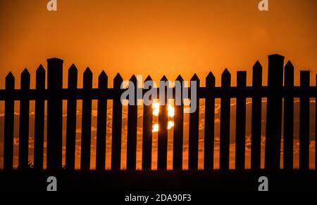 Sonnenuntergang und ein Zaun. Generisches Foto der Sonneneingangsaufnahme durch einen Pfostenzaun. Stockfoto