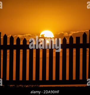 Sonnenuntergang und ein Zaun. Generisches Foto der Sonneneingangsaufnahme durch einen Pfostenzaun. Stockfoto