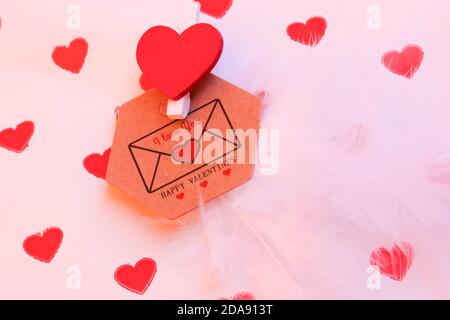 Brauner Umschlag mit einer Liebesnote für einen Liebsten am Valentinstag, die Inschrift I love you auf dem Hintergrund von Geschenkpapier mit kleinen roten Herzen, Stockfoto