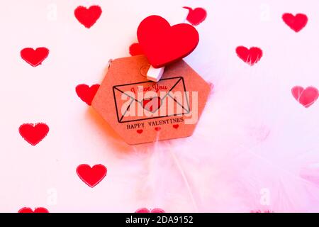 Brauner Umschlag mit einer Liebesnote für einen Liebsten am Valentinstag, die Inschrift I love you auf dem Hintergrund von Geschenkpapier mit kleinen roten Herzen, Stockfoto
