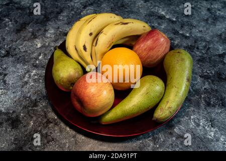 Nahaufnahme von Früchten, Bananen, Birnen, Äpfeln und Orange in rotem Tablett auf dem Tisch Stockfoto