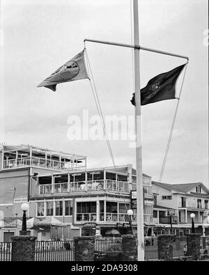 Zwei Flaggen im Wind auf einem Mast vor einem Restaurant in der Nebensaison auf der Promenade von Hampton Beach New Hampshire. Das Bild Stockfoto